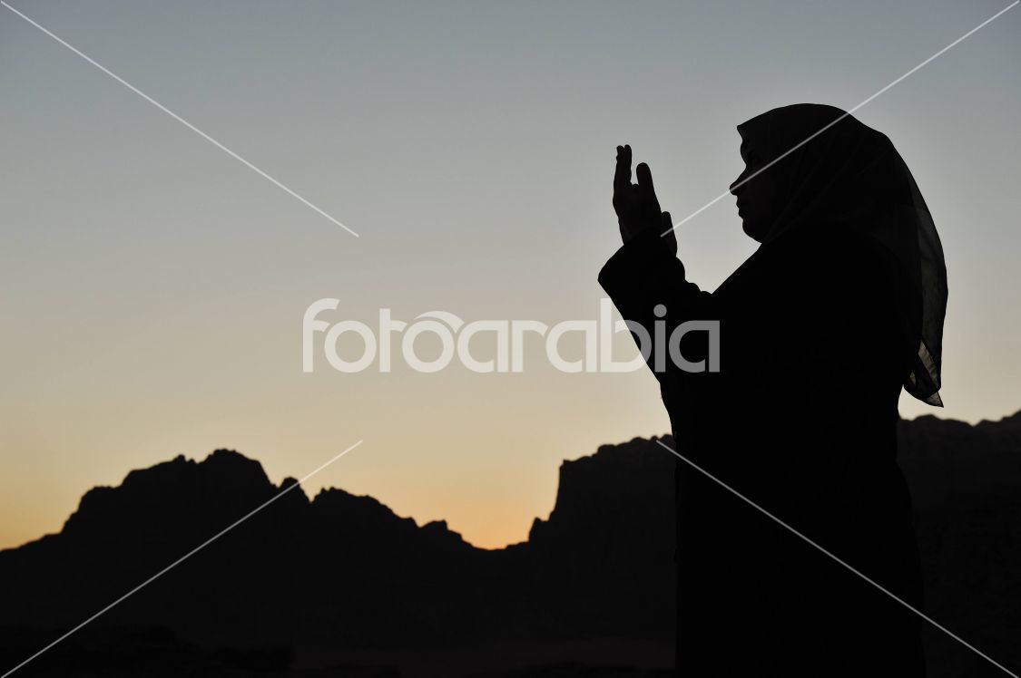 silhouette of a muslim woman praying on the desert