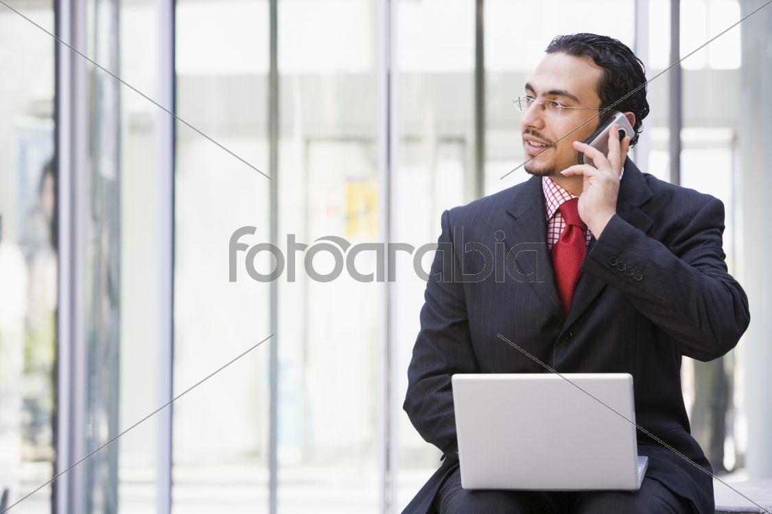 Businessman using laptop and mobile phone outside