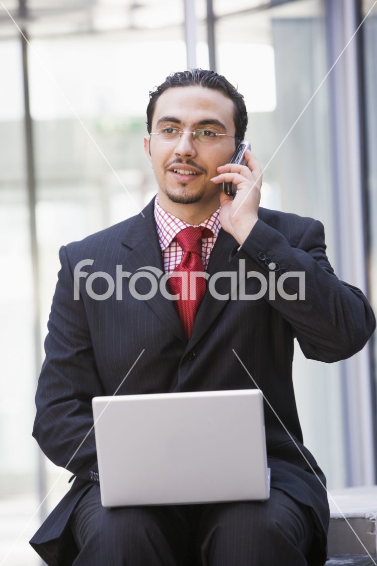 Businessman using laptop and mobile phone outside