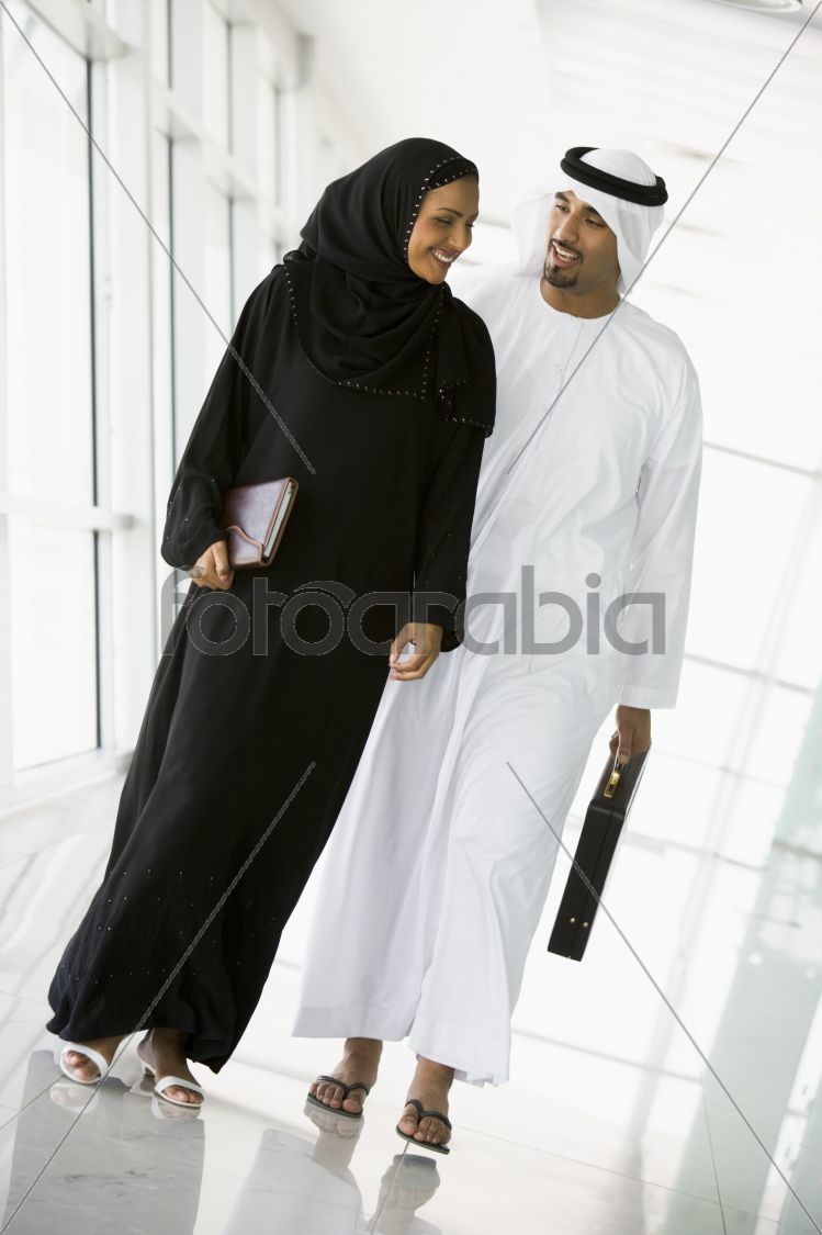 A Middle Eastern businessman and businesswoman walking down a co